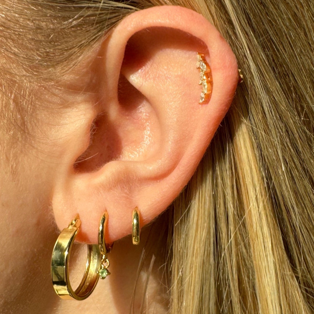 Close-up of an ear wearing gold hoop earrings with small gemstones.