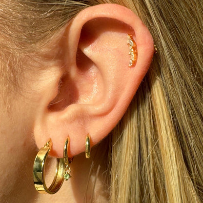 Close-up of an ear wearing gold hoop earrings with small gemstones.
