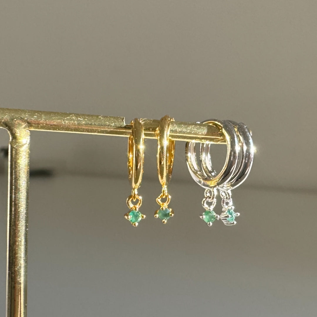 Gold and silver hoop earrings with green gemstones on a gold jewellery tree with a grey background